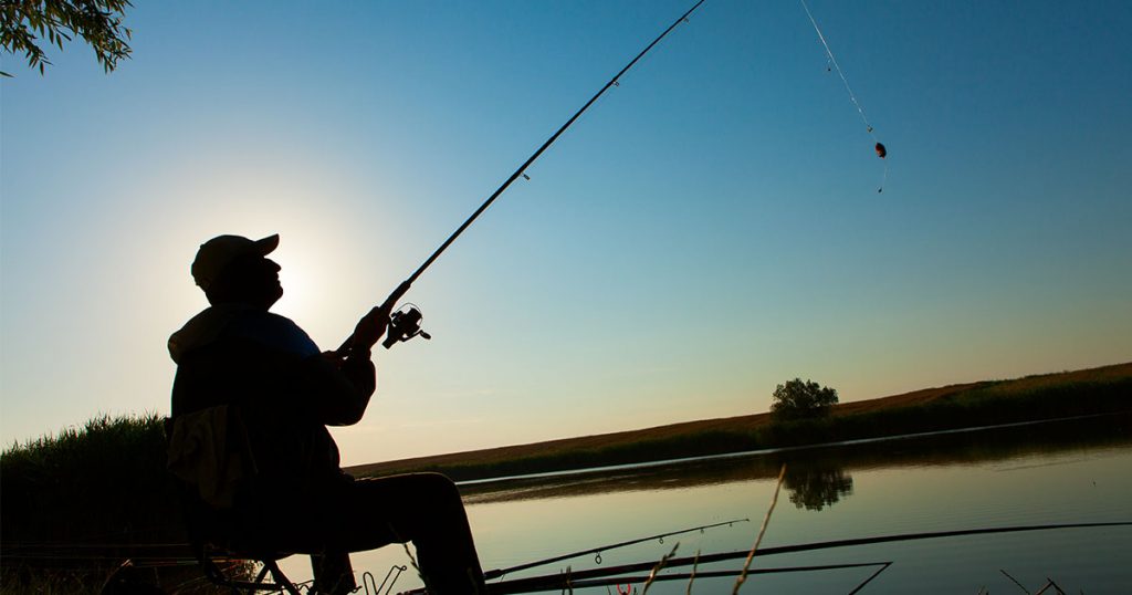 Férfi horgászik a tavon lemenő napnál