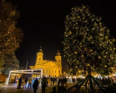Kivilágított karácsonyfa és adventi vásár a Kossuth téren, háttérben a Nagytemplom