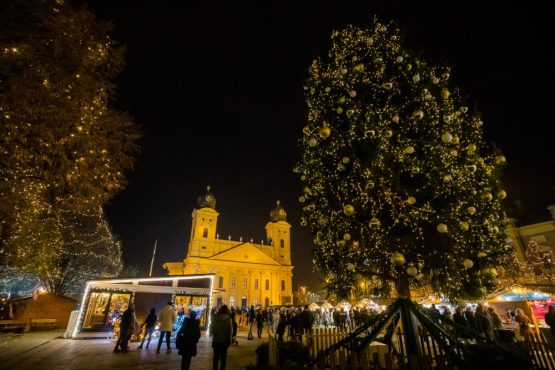 Kivilágított karácsonyfa és adventi vásár a Kossuth téren, háttérben a Nagytemplom