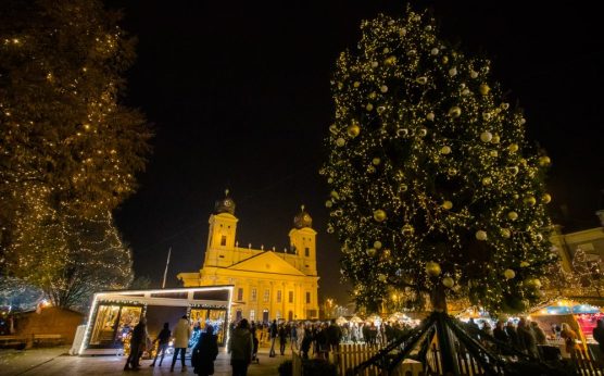 Kivilágított karácsonyfa és adventi vásár a Kossuth téren, háttérben a Nagytemplom