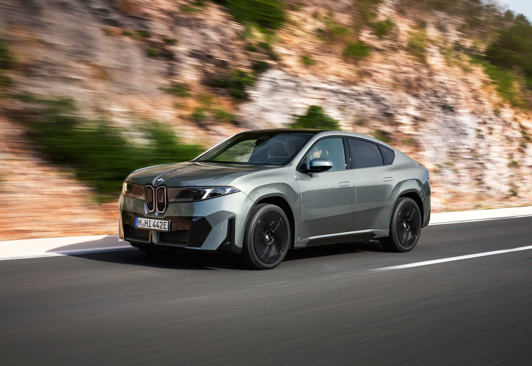 Szürke BMW iX4 menet közben, sziklafal mellett