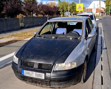 Szélvédő nélküli ezüst személyautó egy rendőrautó előtt Debrecenben, kitakart rendszámmal