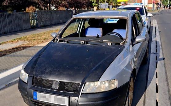 Szélvédő nélküli ezüst személyautó egy rendőrautó előtt Debrecenben, kitakart rendszámmal