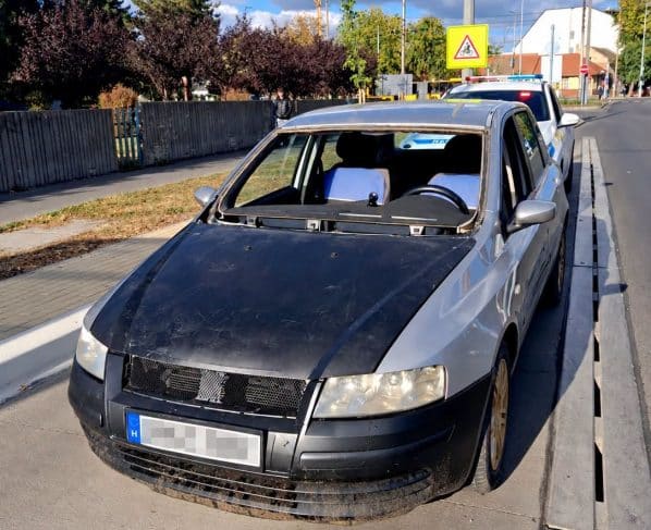 Szélvédő nélküli ezüst személyautó egy rendőrautó előtt Debrecenben, kitakart rendszámmal